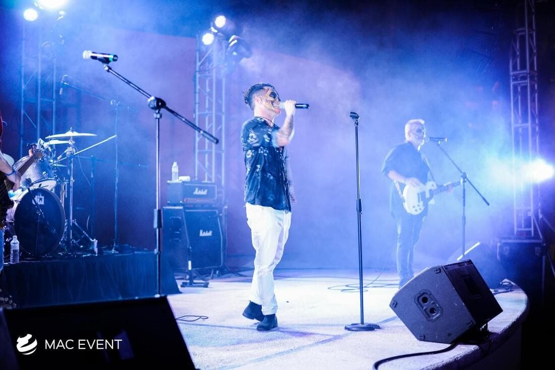A band performs live on stage with dynamic blue and white lighting, as the lead singer engages with the audience in a vibrant concert atmosphere.